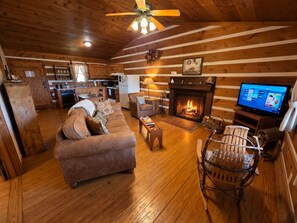 Ein gemütliches Blockhauss-Interieur mit Wohnzimmer, Kamin, Fernseher und Küchenzeile.