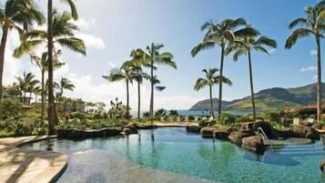 Un espace piscine aménagé dans un complexe hôtelier, avec une eau cristalline, entouré de palmiers et dominé par un paysage montagneux.