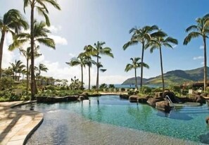 A resort pool area with clear water, surrounded by palm trees and a mountainous backdrop. - Pukalani a Marriott Grand Residence  (Lihue, Kauai)