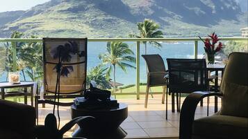 Une terrasse offrant une vue sur les montagnes et la mer, aménagée avec des chaises et une table, et agrémentée d’un vase de fleurs.