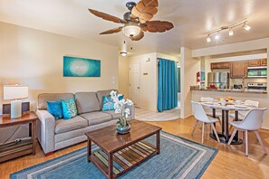 A modern living room with a ceiling fan, a dining area with a table and chairs, and a kitchen visible through an open door. - Charming Kihei Condo Private Lanai Pool Hot Tub Steps to Whale Sanctuary (Kihei)
