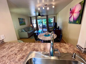 A kitchen with a stainless steel sink, a dining area with a round table and chairs, a sofa, and a television.