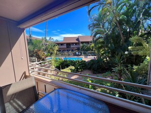 A balcony with a view of a swimming pool, surrounded by lush greenery and palm trees.
