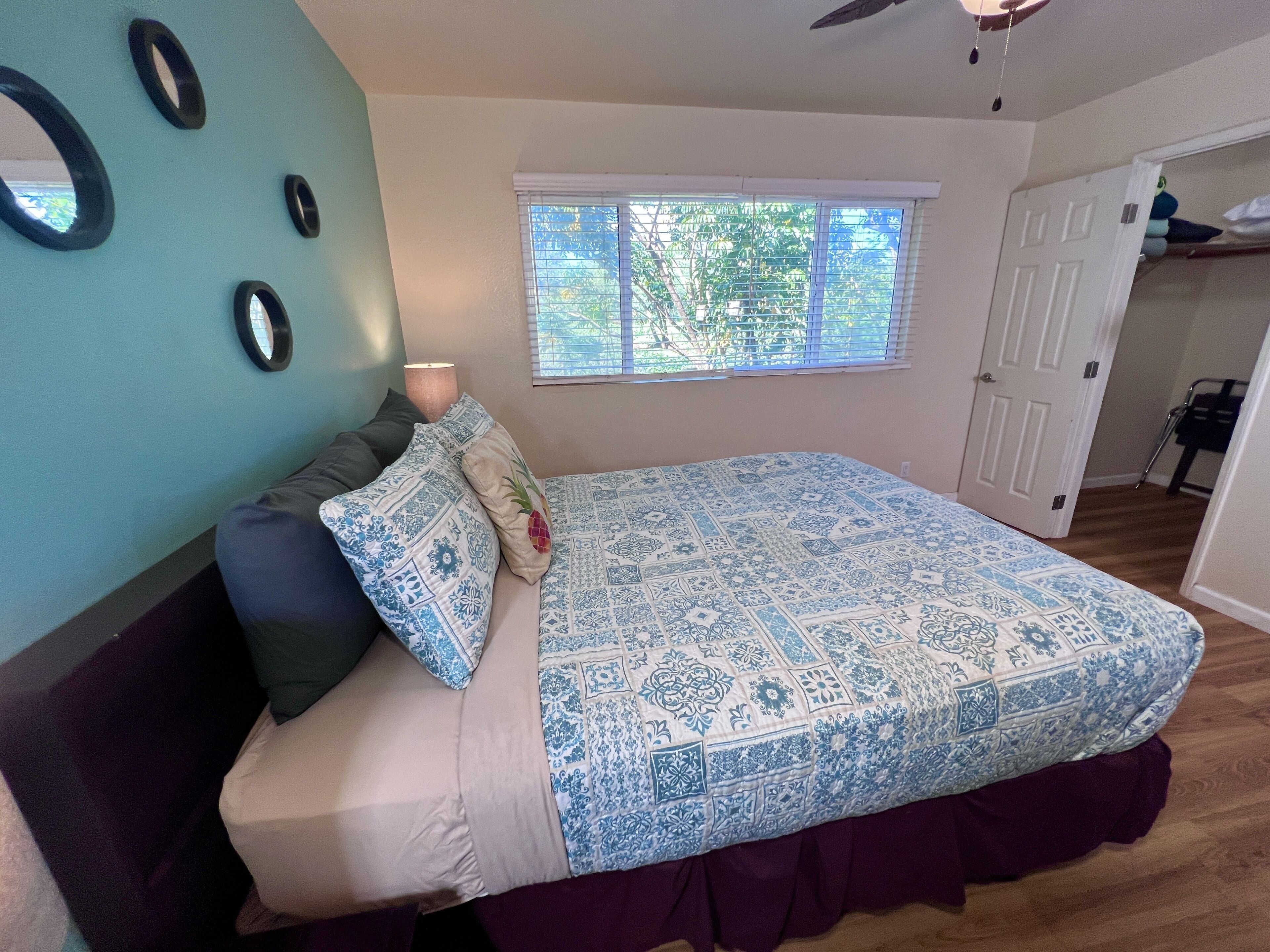 A bedroom with a bed, a window with blinds, a door, and a ceiling fan.