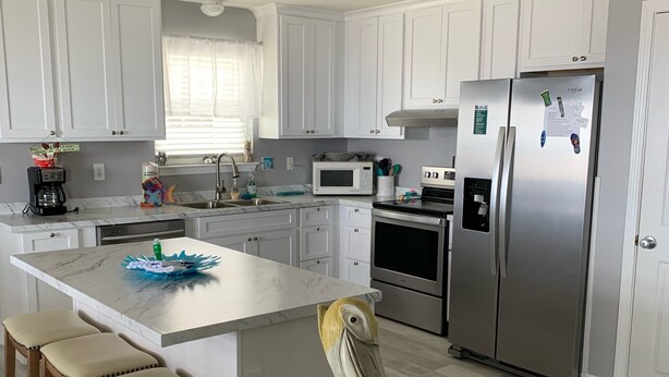 Una cocina moderna con armarios blancos, una isla central con taburetes, un refrigerador de acero inoxidable y una escultura decorativa de pelícano.