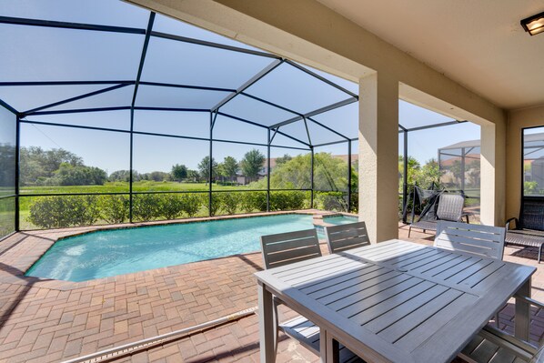 A covered outdoor swimming pool with a patio area, including a table and chairs, and a view of a green landscape. - Disney 7BR Villa w/ Pool, Spa & Lazy River! (Davenport)