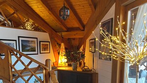 A wooden staircase with patterned tiles leading to a dark room with a fireplace, framed pictures on the wall, and a decorative plant.