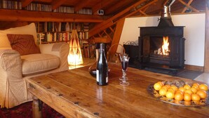 A cozy loft living room with a fireplace, wooden beams, a sofa, a coffee table, a bookshelf, and a fruit bowl.