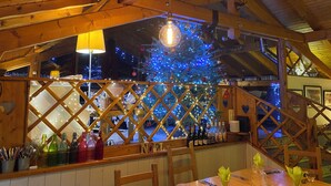 A cozy restaurant with a wooden interior, a Christmas tree adorned with lights, and a view of the snowy outdoors.