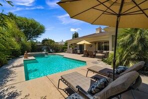 Un jardin avec une piscine, des chaises longues et un espace patio aménagé avec du mobilier d’extérieur.