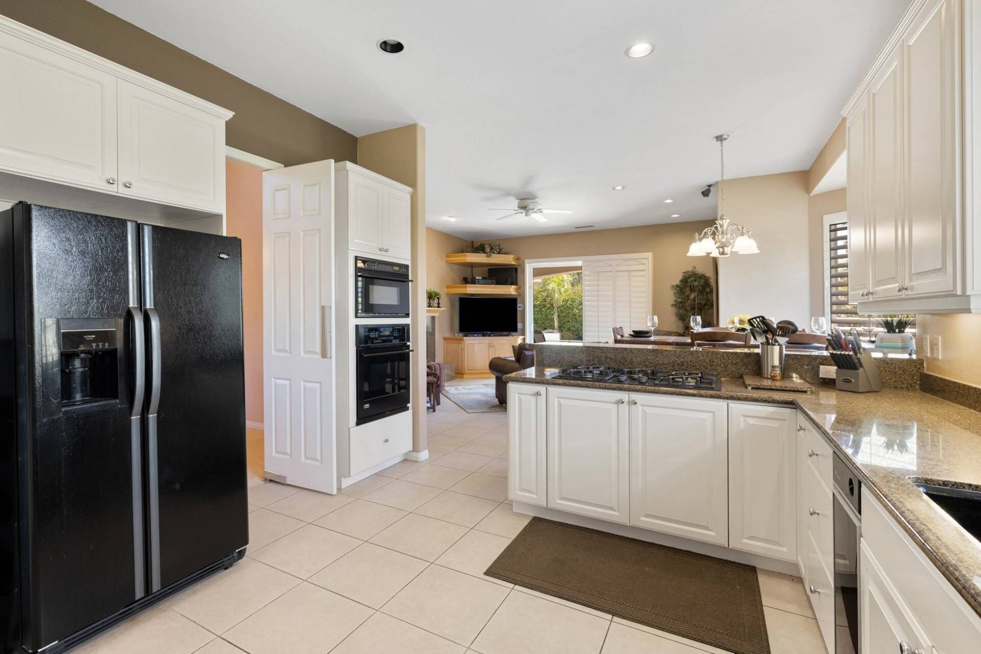 A modern kitchen with white cabinetry, a black refrigerator, a built-in oven, and a central island with a stove.