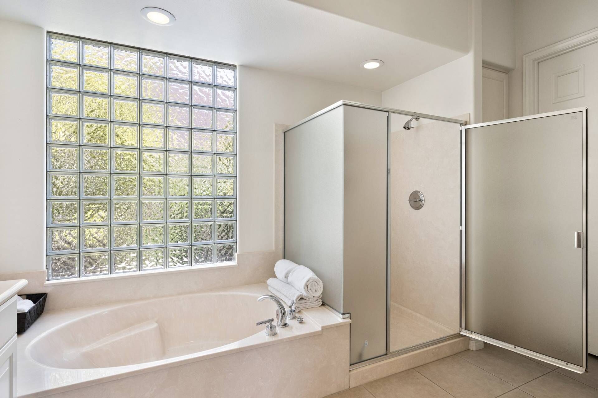 Ein modernes Badezimmer mit freistehender Badewanne, einer Duschkabine aus Glas und einem großen Fenster mit Blick auf Bäume.