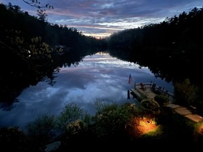 A serene lake with a wooden dock and an American flag, surrounded by dense forest. - Lake Sequoyah Cottage: Lakeside Retreat w/ Hot Tub, Dock & Canoe | Pet-Friendly (Highlands)