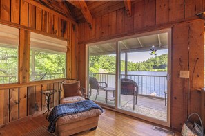 L'intérieur d'un chalet en bois, avec un canapé, une petite table et une vue sur un lac, visible à travers une porte-fenêtre coulissante.