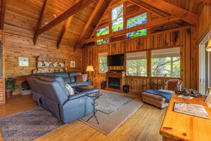 A cozy cabin interior with a fireplace, leather sofa, and a television.