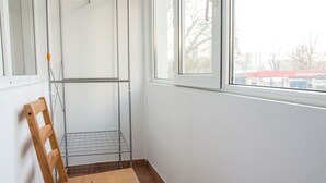 Habitación en esquina con una silla de madera, una estantería de metal y una ventana con vistas a edificios.