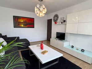 A modern living room with a white sofa, a coffee table, a television, and a painting on the wall. - Tineretului 20 by MRG Apartments | Tineretului Park | City Centre | Metro (București)