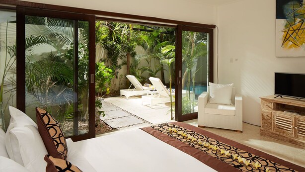 A bedroom with a large bed, a TV, and a view of a pool and outdoor seating area. - 50meter from Seminyak beach,2BR Villa  (Seminyak)