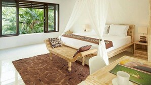 A bedroom with a canopy bed, a wooden bench, a small table with a cup, and a view of greenery through large windows. - 50meter from Seminyak beach,2BR Villa  (Seminyak)