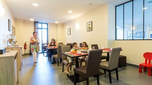 Uma área de refeições com mesas e cadeiras, um balcão com um registrador de caixa e um extintor de incêndio na parede.