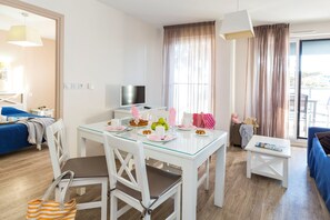 A modern, well-lit room with a dining table set for breakfast, a TV, and a sofa.