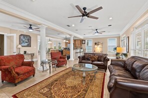 Ein geräumiges Wohnzimmer mit großem Teppich, Ledersofas, einem Glastisch und Deckenventilatoren.