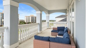 Een overdekt balkon met witte balustrades, rieten meubilair en uitzicht op omliggende gebouwen.