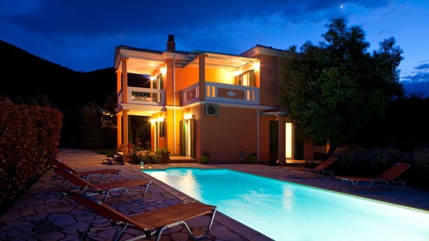 A two-story house with a swimming pool, lounge chairs, and a well-lit exterior. - VILLA PANTHEON, SYVOTA BAY, LEFKADA (SYVOTA LEFKADA)