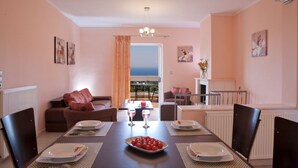 A dining area with a table set for four, a view to the outside, and a cozy seating arrangement with a sofa and chairs. - VILLA PANTHEON, SYVOTA BAY, LEFKADA (SYVOTA LEFKADA)
