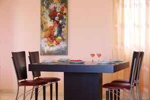 A dining area with a table set for two, surrounded by four chairs. A painting is on the wall above the table.