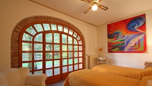 A room with a large arched window, a ceiling fan, a bed with a quilted cover, a chair, and a colorful abstract painting on the wall. - Holiday Home for 5 People, Garden, 500m till Sea, A/C, WIFI, near Forte dei Marmi (Marina Dei Ronchi)