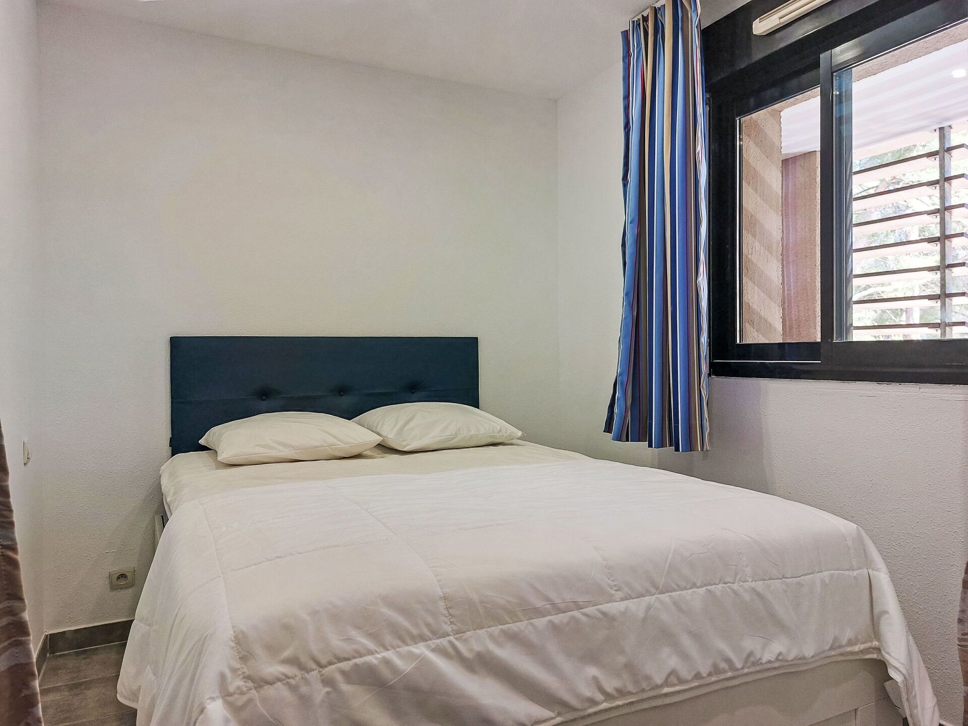 Une chambre à coucher avec un lit, une fenêtre ornée de rideaux à rayures et une vue sur l’extérieur.