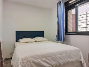 Ein Schlafzimmer mit Bett, Fenster mit gestreifter Vorhang und Blick nach draußen.
