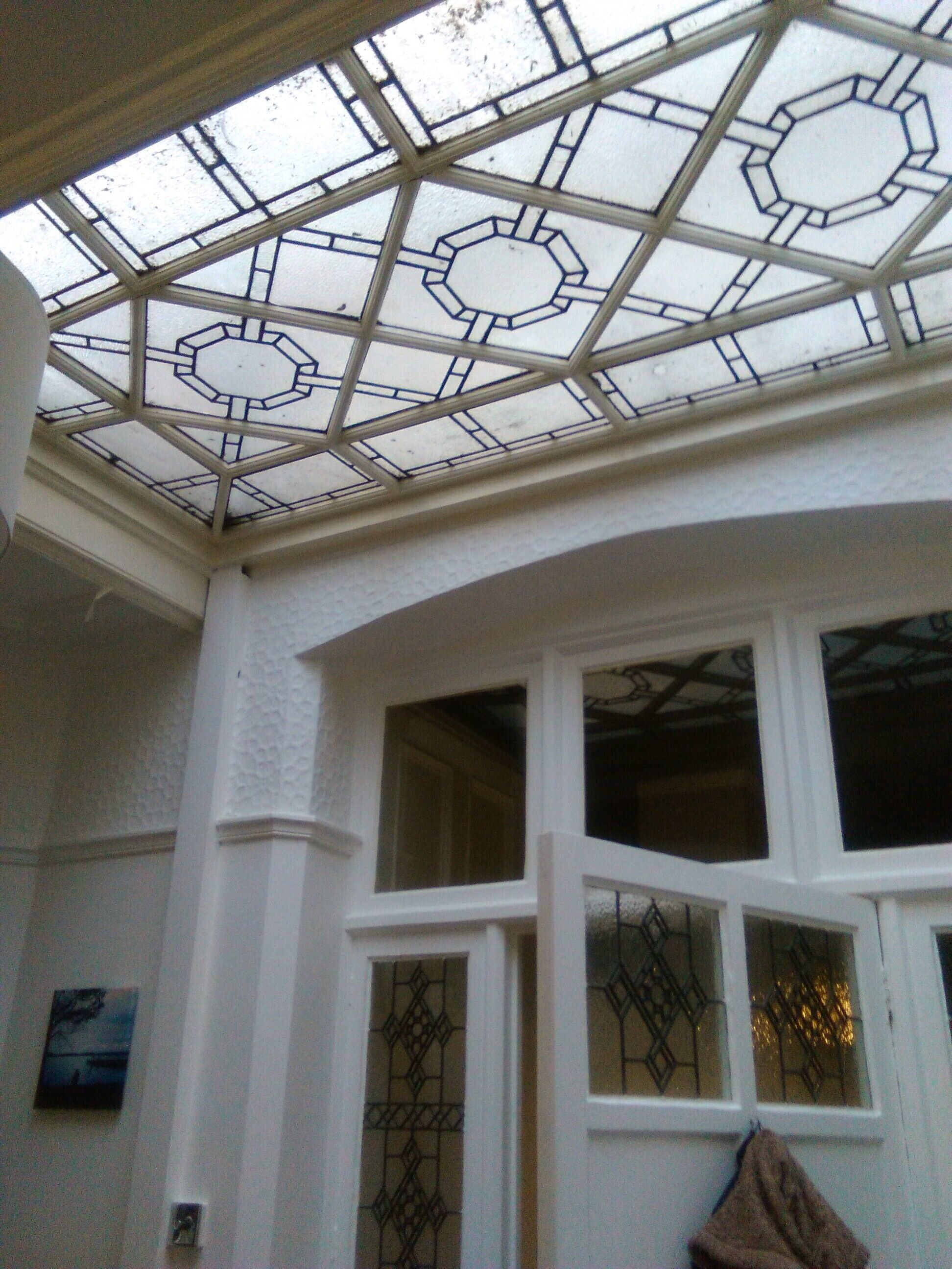 Ett rum med ett takfönster som har geometriska mönster i färgat glas, vita väggar och en dörr med dekorativa glaspaneler.