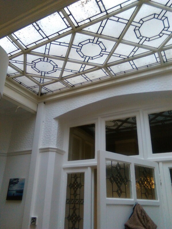 A room with a skylight featuring geometric stained glass patterns, white walls, and a door with decorative glass panels.