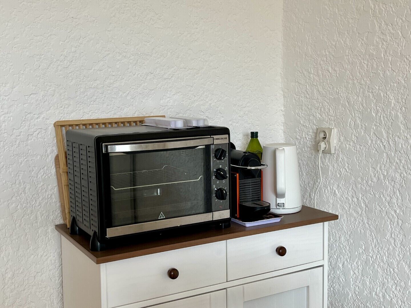 Eine Küchenzeile mit integriertem Mikrowellenherd und Toasterofen, ein weißes Schränkchen mit zwei Schubladen und eine weiße Wand.