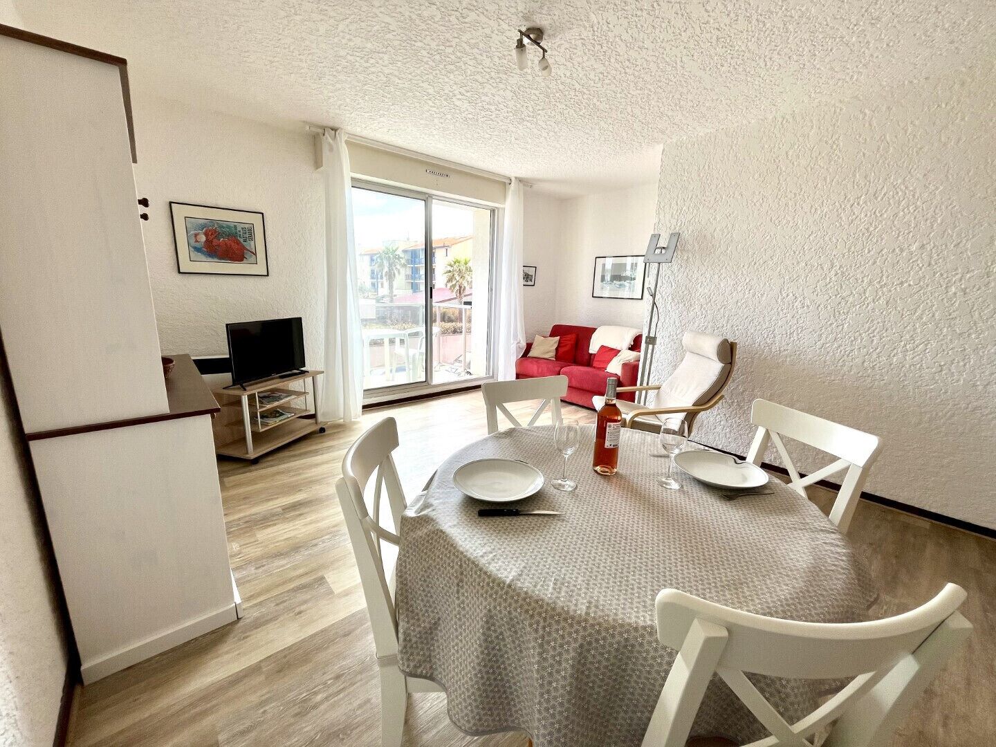 A dining area with a table set for two, a television, and a red couch in the background.