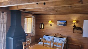 A cozy cabin interior with a wooden dining table, chairs, a bench with patterned cushions, a fireplace, and wall-mounted lamps. - Charming 2-bedroom half chalet with terrace, Pra Loup (Pra-Loup)