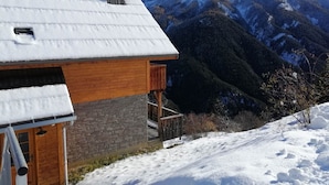 A wooden chalet with a stone foundation, a balcony, and a view of snow-covered mountains. - Charming 2-bedroom half chalet with terrace, Pra Loup (Pra-Loup)