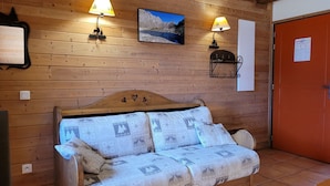 A wooden cabin room with a wooden bed, two wall-mounted lamps, a framed picture, and a door with a notice. - Charming 2-bedroom half chalet with terrace, Pra Loup (Pra-Loup)