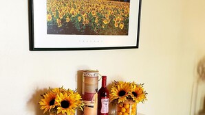 Une table blanche sur laquelle est posée une peinture encadrée, deux vases contenant des tournesols, une bouteille et un magazine.