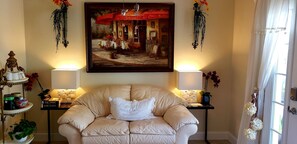 Relax in this inviting living room with a sofa, lamps, and a beautiful painting above.