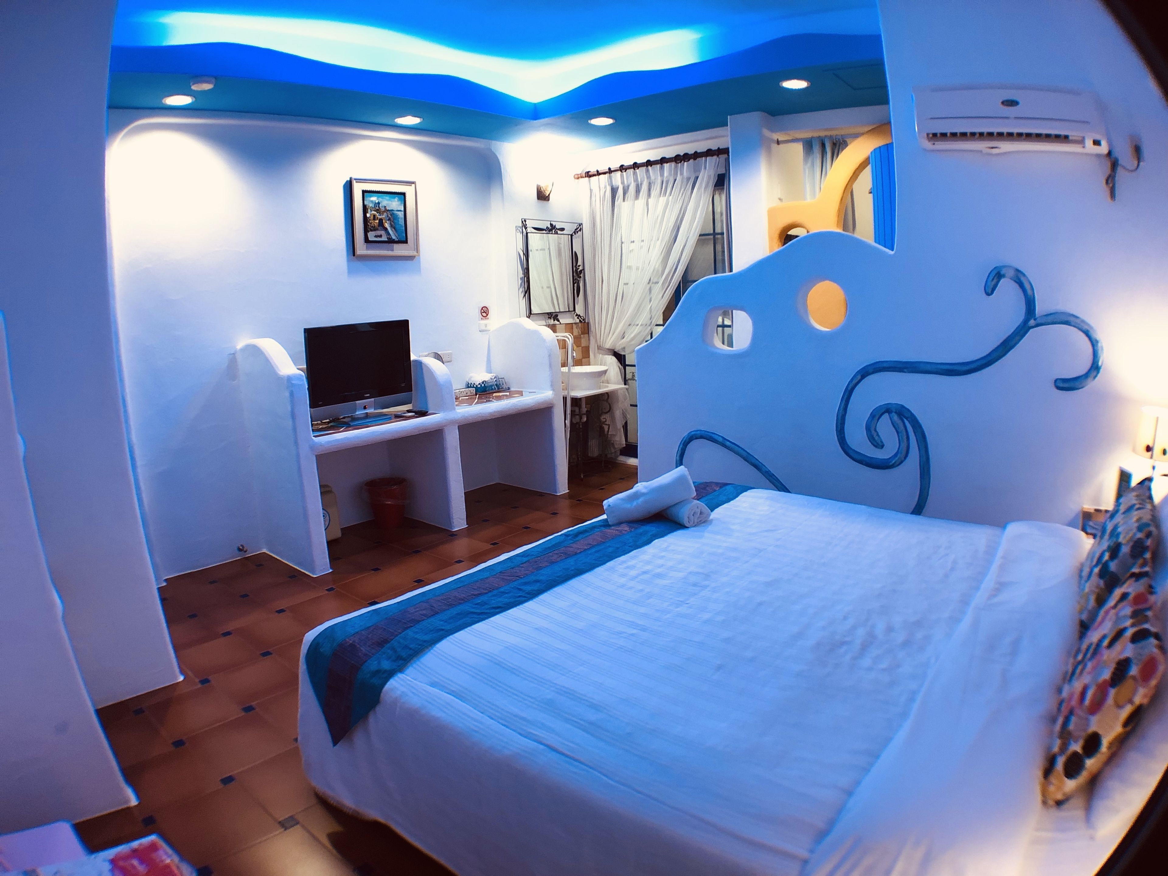Un dormitorio con cama, escritorio, televisor y baño.