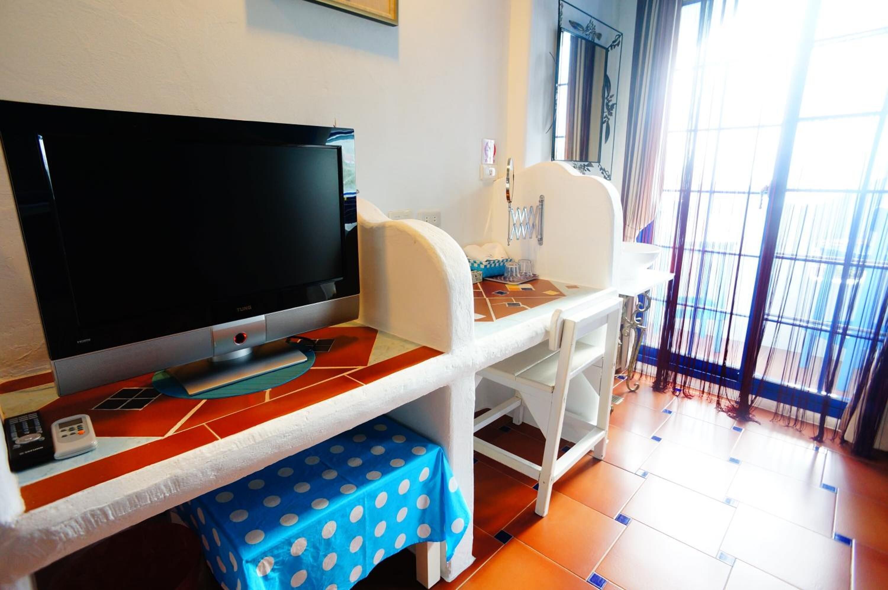 Una habitación con televisión de pantalla plana, una mesita con mantel de lunares y una silla.