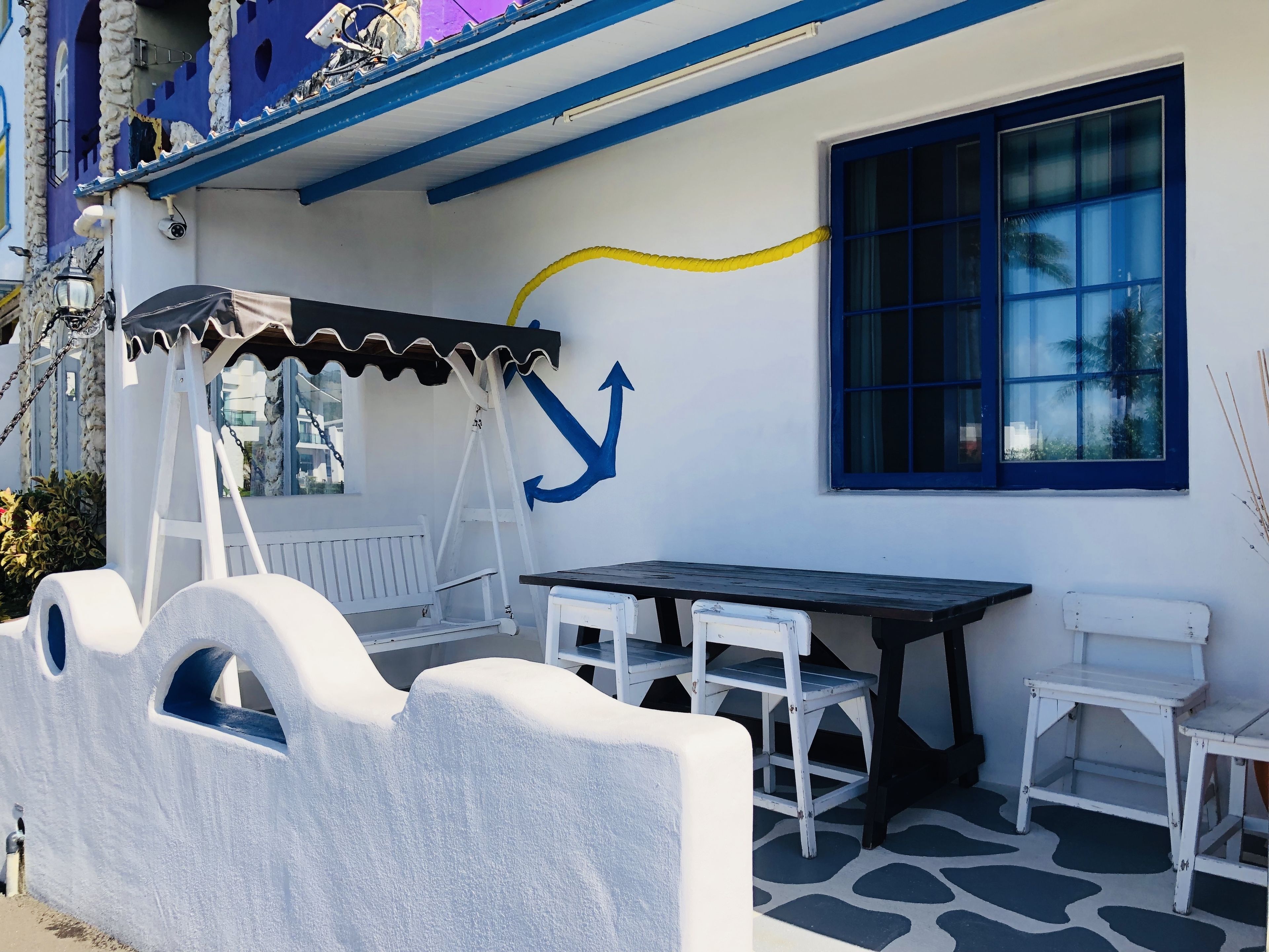 A patio area with a table and chairs, a swing, and a wall with a blue anchor decoration.