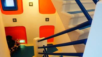 Una escalera con barandas azules y peldaños blancos, que lleva a una habitación con paredes anaranjadas y un ventanal pequeño.