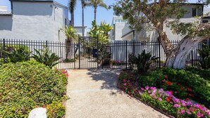 A gated entrance to a residential area with a gravel pathway, surrounded by lush greenery and flowering plants. - Across the street from the beach in Del Mar!  1757 Coast Blvd (Del Mar)
