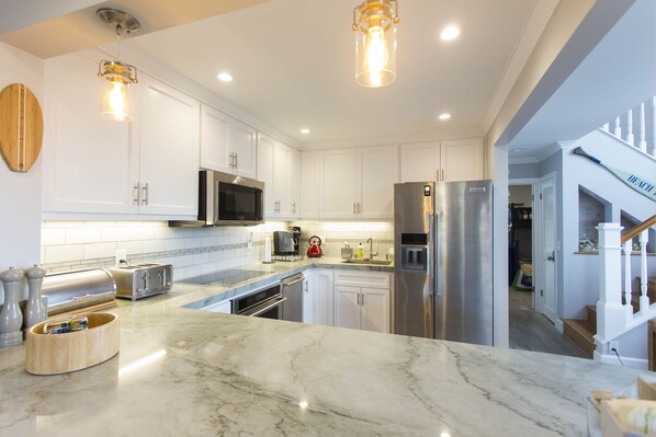 A modern kitchen with white cabinets, stainless steel appliances, and a marble countertop.