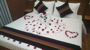 A neatly made bed with rose petals arranged in a heart shape and a swan design, a decorative pillow, and a patterned bedspread. - Grand Diamond Guest House (Mingaladon Township)