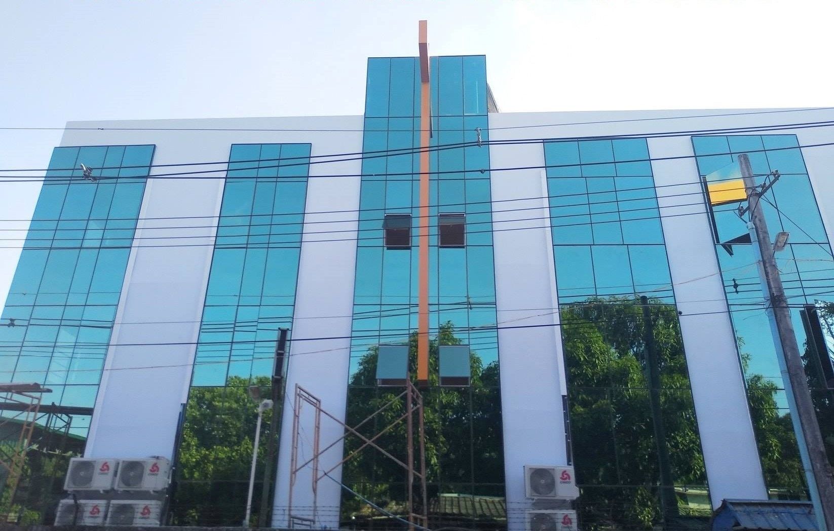 A modern building with a glass facade, multiple air conditioning units, and a central vertical structure.